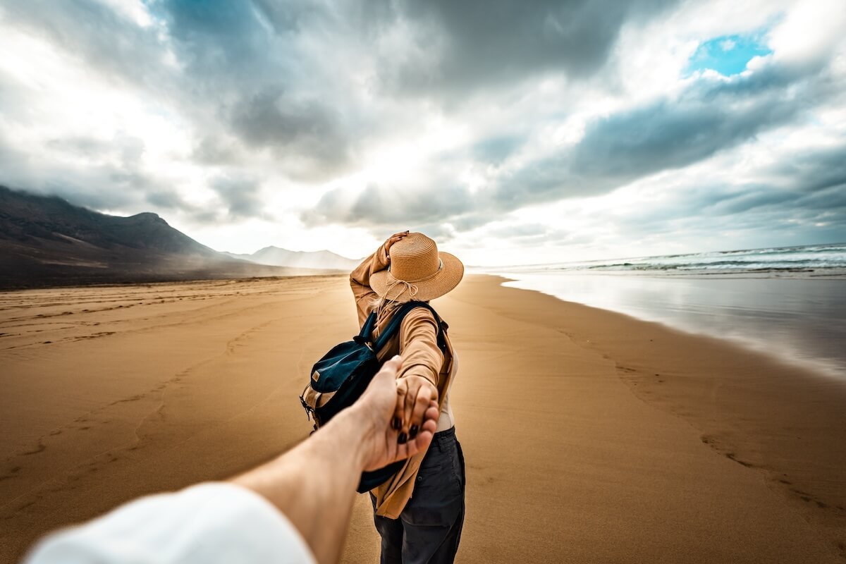 Shutterstock: Happy and excited girl taking her boyfriend's hand while walking enjoying summer sunset at the beach - Traveler couple leads on vacation between the mountain - Follow me concept and traveling together