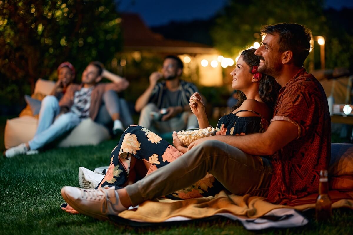 Shutterstock: Happy couple watching movie with friends in the backyard at night.