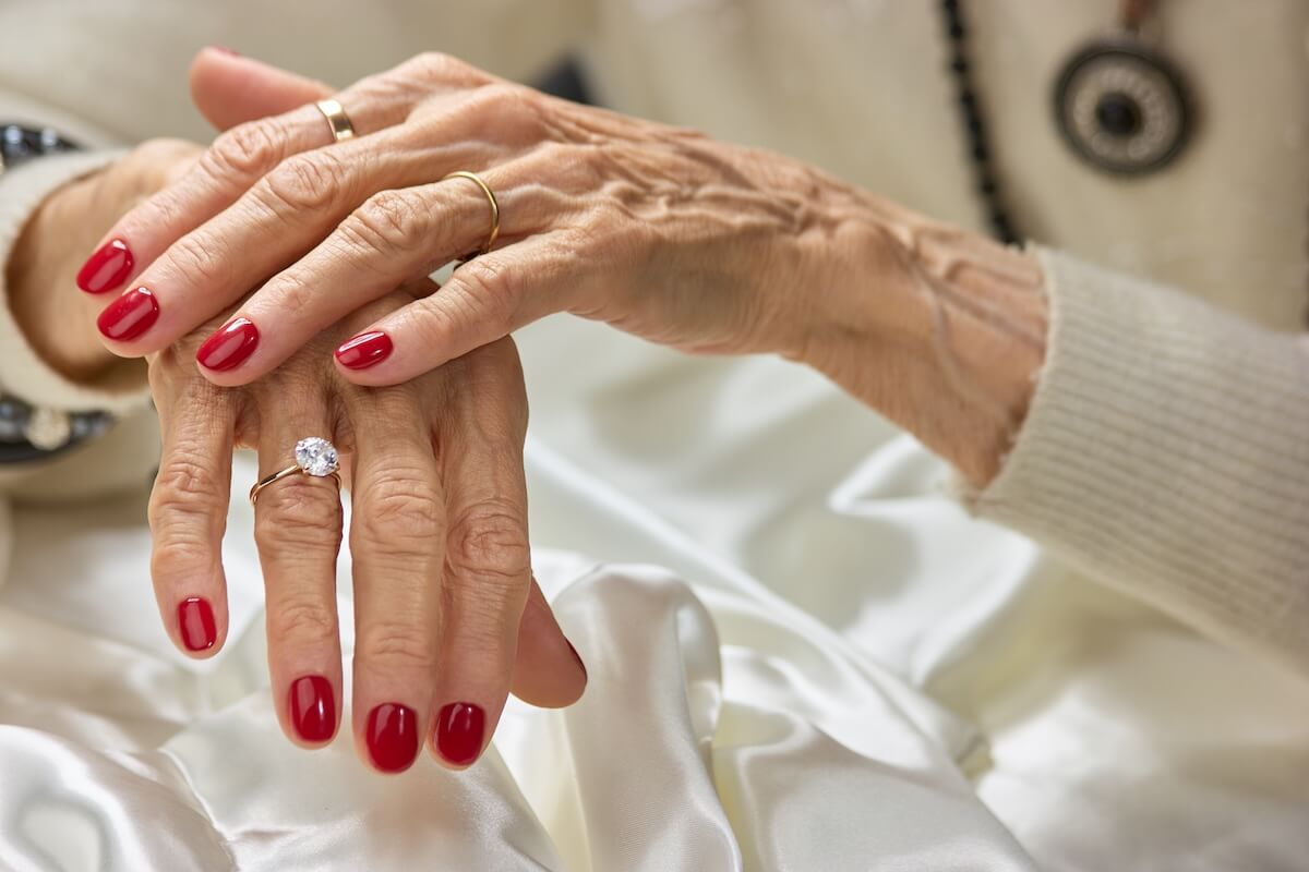 Shutterstock: Old woman beautiful hands with rings. Female aged hands with red nails wearing luxury golden rings. Womens aristocratism and well-being.