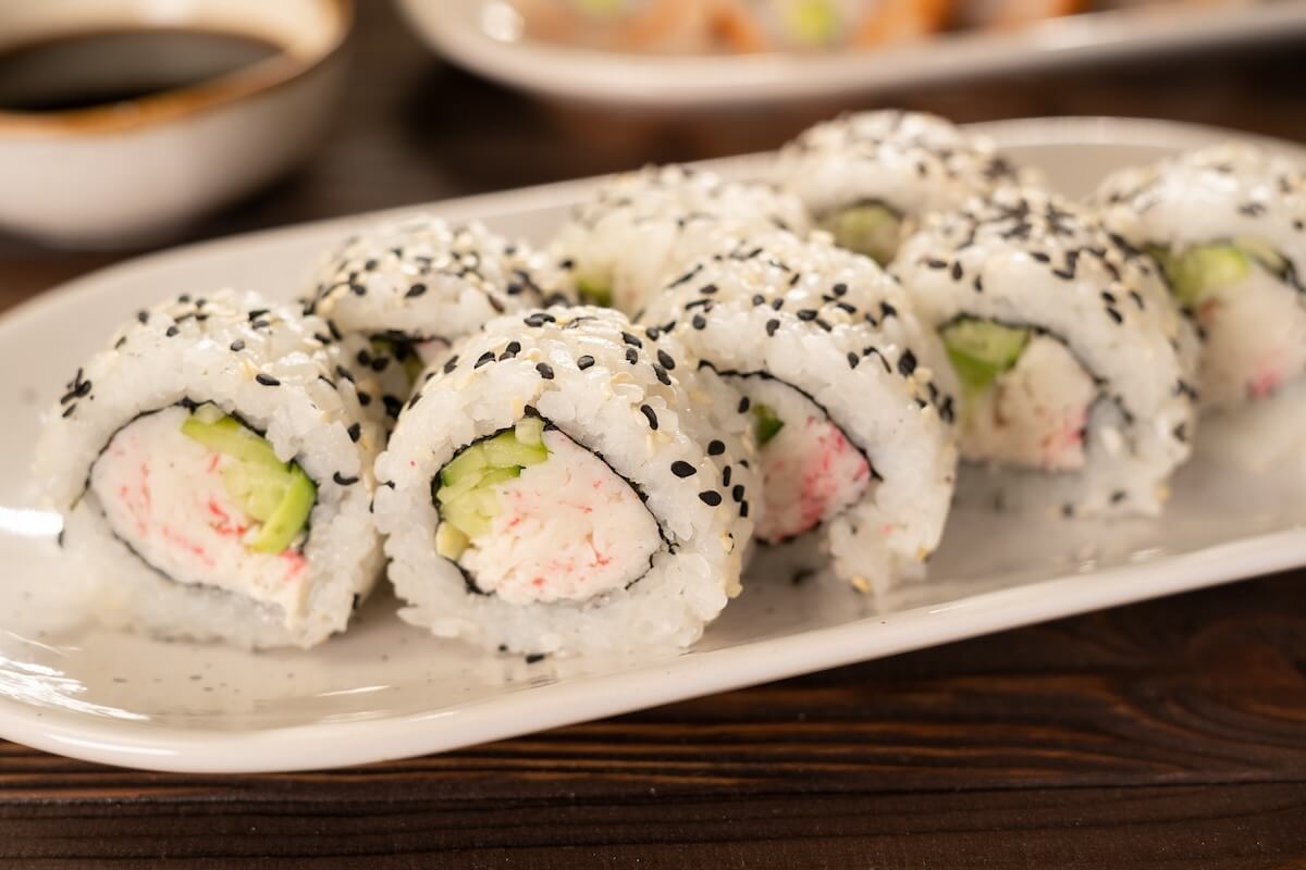 Shutterstock: A set of fresh sushi rolls with crab surimi, avocado and black sesame seeds served on a plate. Japanese sushi uramaki or California roll. Sushi menu. Japanese food concept