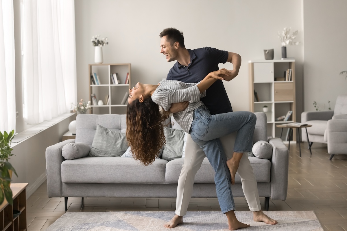 Shutterstock: Happy active married couple dancing in stylish living room interior, enjoying activity at home together. Positive strong husband embracing wife in romantic social dance with passion