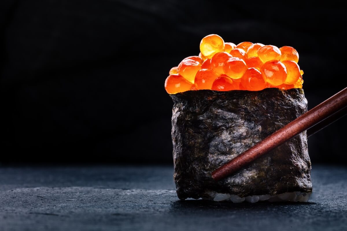 Shutterstock: Ikura sushi maki roll with chopsticks on a black background, with copy space