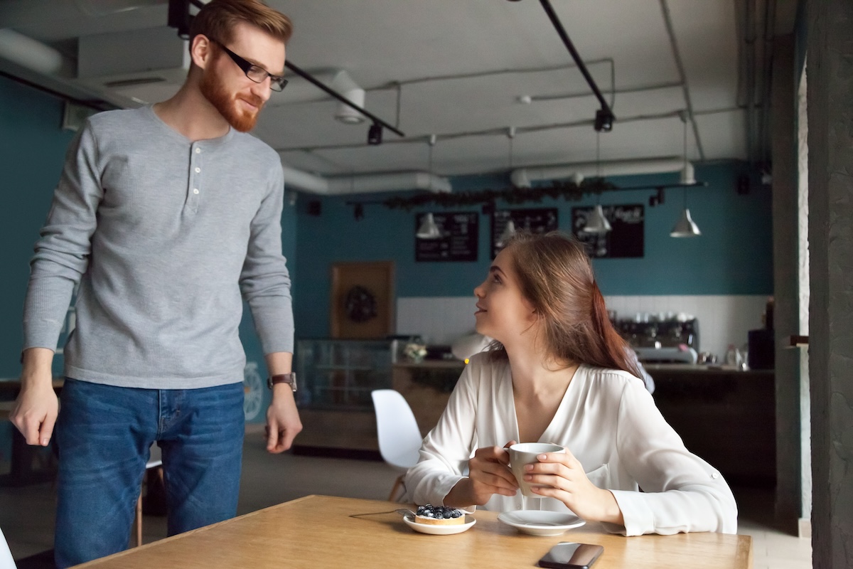 Shutterstock: Young man coming to cafe table getting acquainted with beautiful woman he liked, millennial charming guy flirting chatting with young attractive lady asking on romantic date, first impression concept