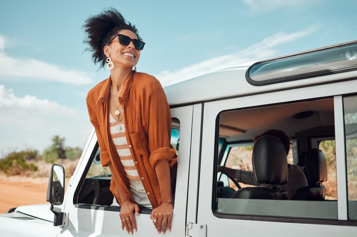Shutterstock: Black woman on road, enjoying window view of desert and traveling in suv on holiday road trip of South Africa. Travel adventure drive, happy summer vacation and explore freedom of nature in the sun