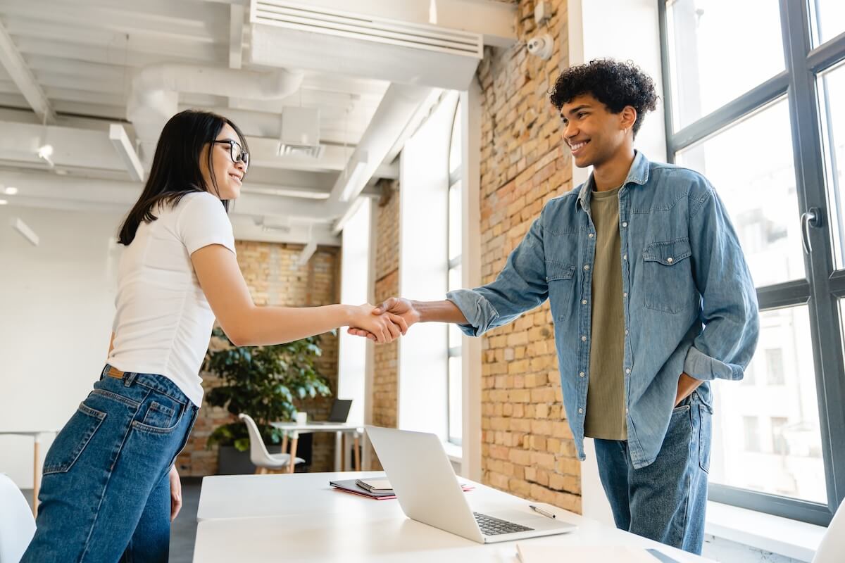 Shutterstock: Cooperative young colleagues students partners friends classmates in smart casual shaking hands have meeting at working desk in office modern coworking collage campus. Partnership cooperation concept