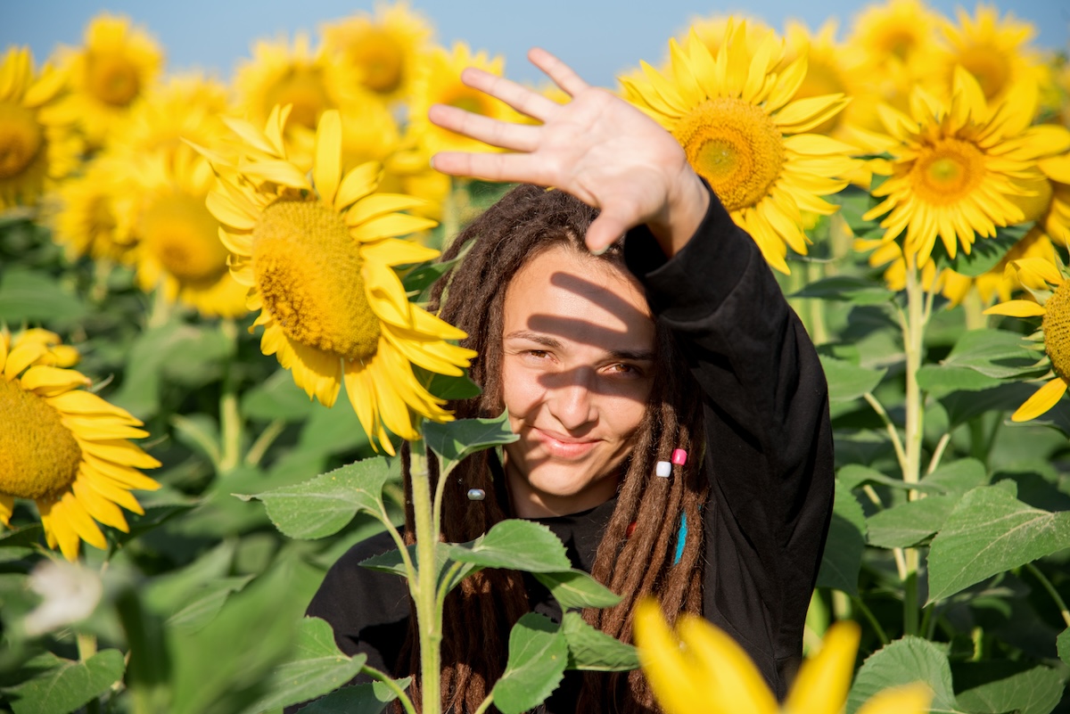 Shutterstock: girl squinted from the sunlight among the sunflowers in the field. A happy hippie with dreadlocks travels in the summer