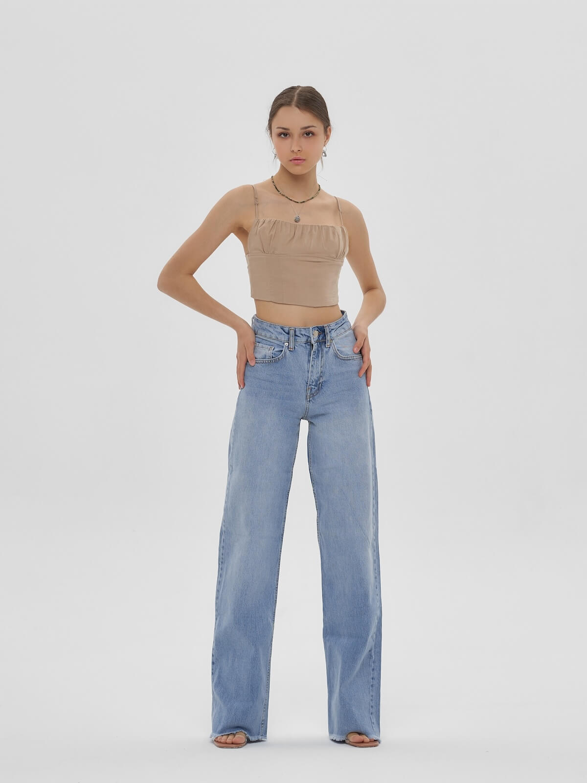 Shutterstock: Young elegant woman with long straight hair and natural make-up in beige top and blue jeans standing and posing on bright grey background