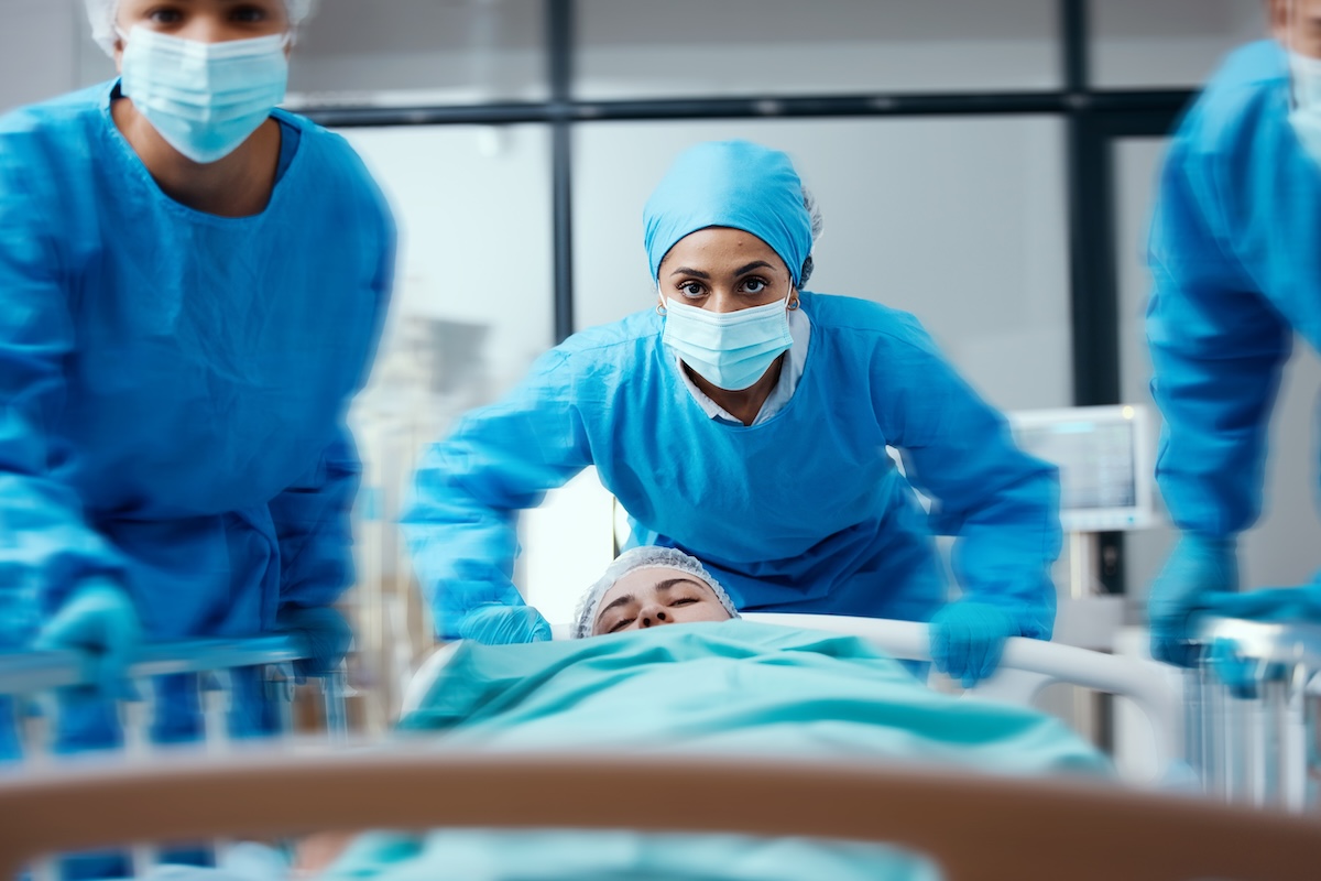 Shutterstock: Surgeon, bed and rush in a hospital for emergency operation in the er with a sick patient. Surgery team, pushing sleeping woman and fast hospital bed in the theater for surgical medicine procedure