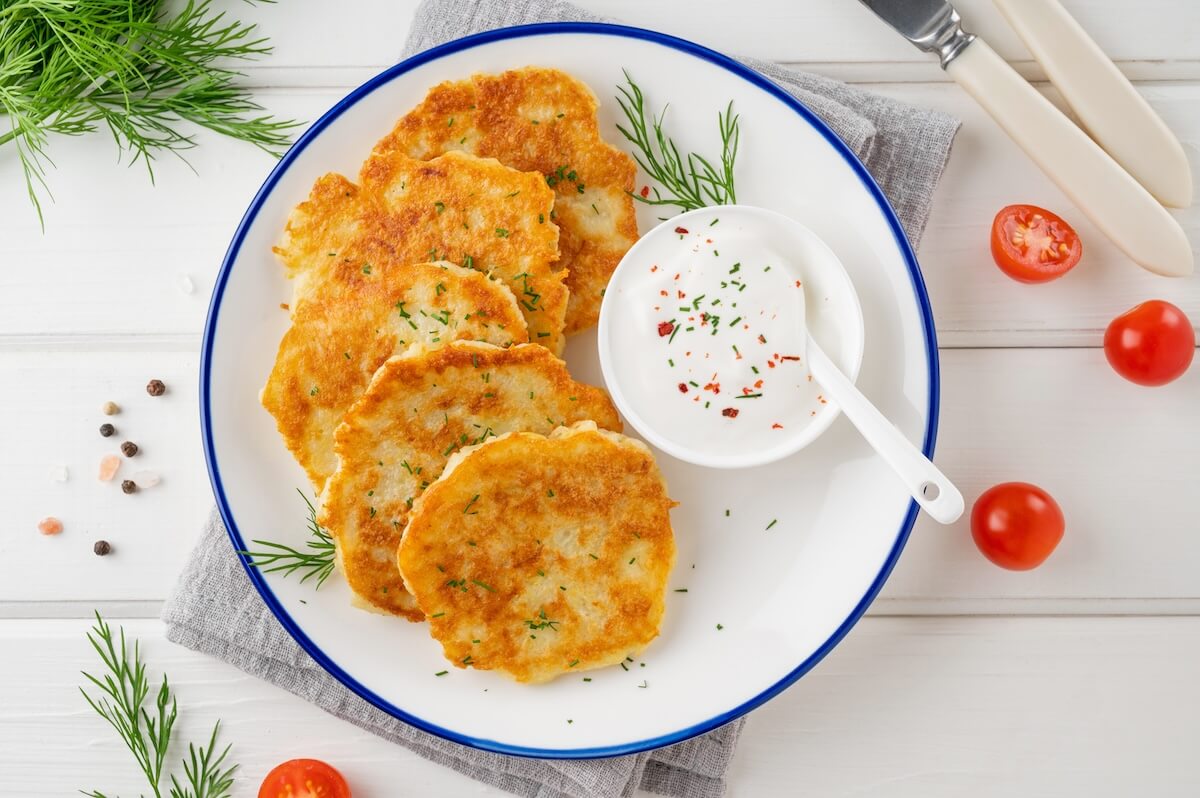 Shutterstock: Potato pancakes, latkes or draniki with fresh herbs and sour cream on a plate on a white wooden background. Top view, copy space