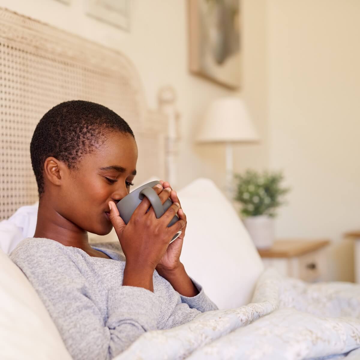 Shutterstock: Young African American woman sitting up in her bed in the morning sipping a cup of coffee