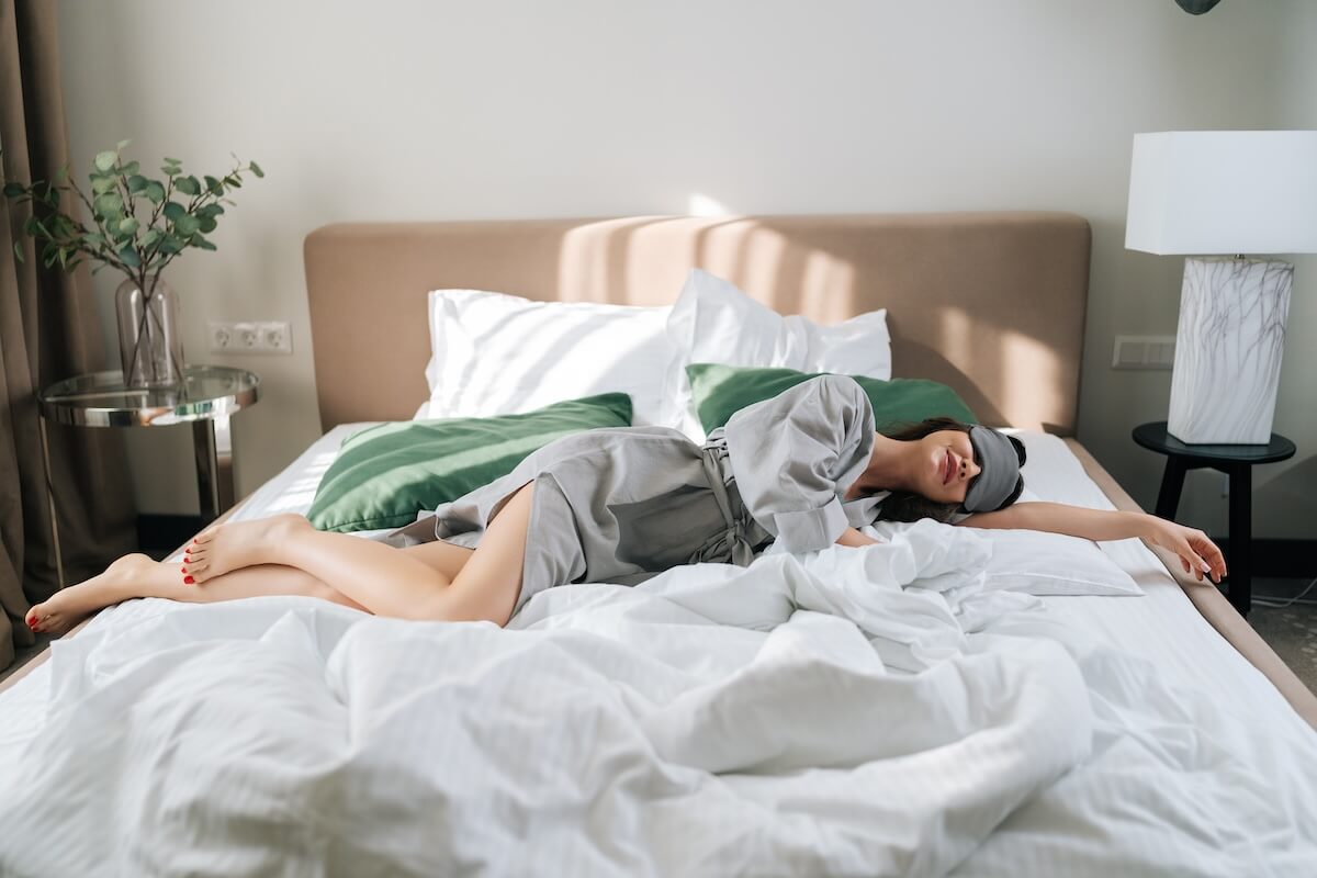 Shutterstock: Wide shot portrait of happy early bird young woman wearing sleeping mask lying in comfy bed in luxury hotel bedroom. Pretty brunette female in pajama waking up enjoy good morning at home.