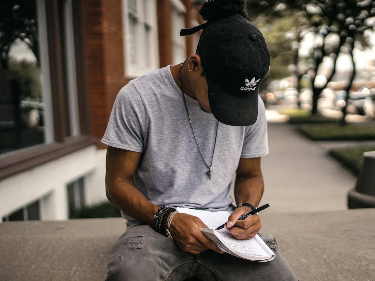 Unsplash: Man writing outside with pen and paper by Brad Neathery