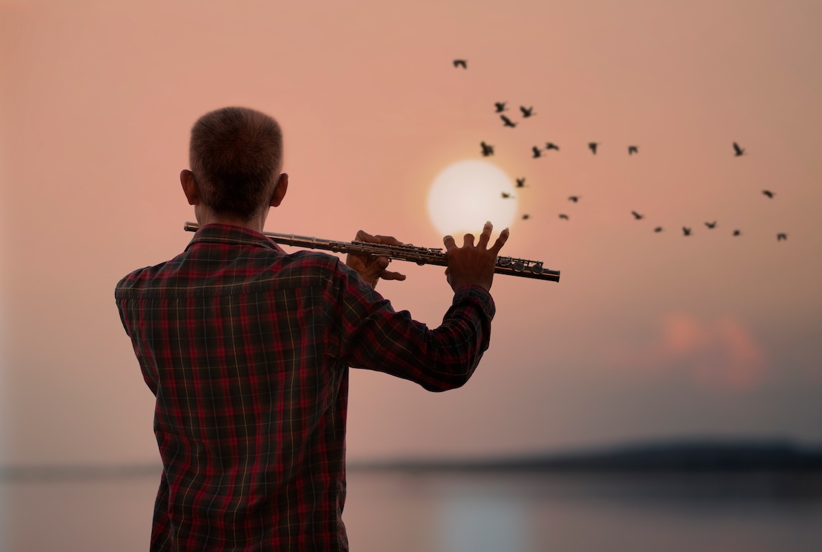 Shutterstock: Man playing flute with sunset or sunrise background