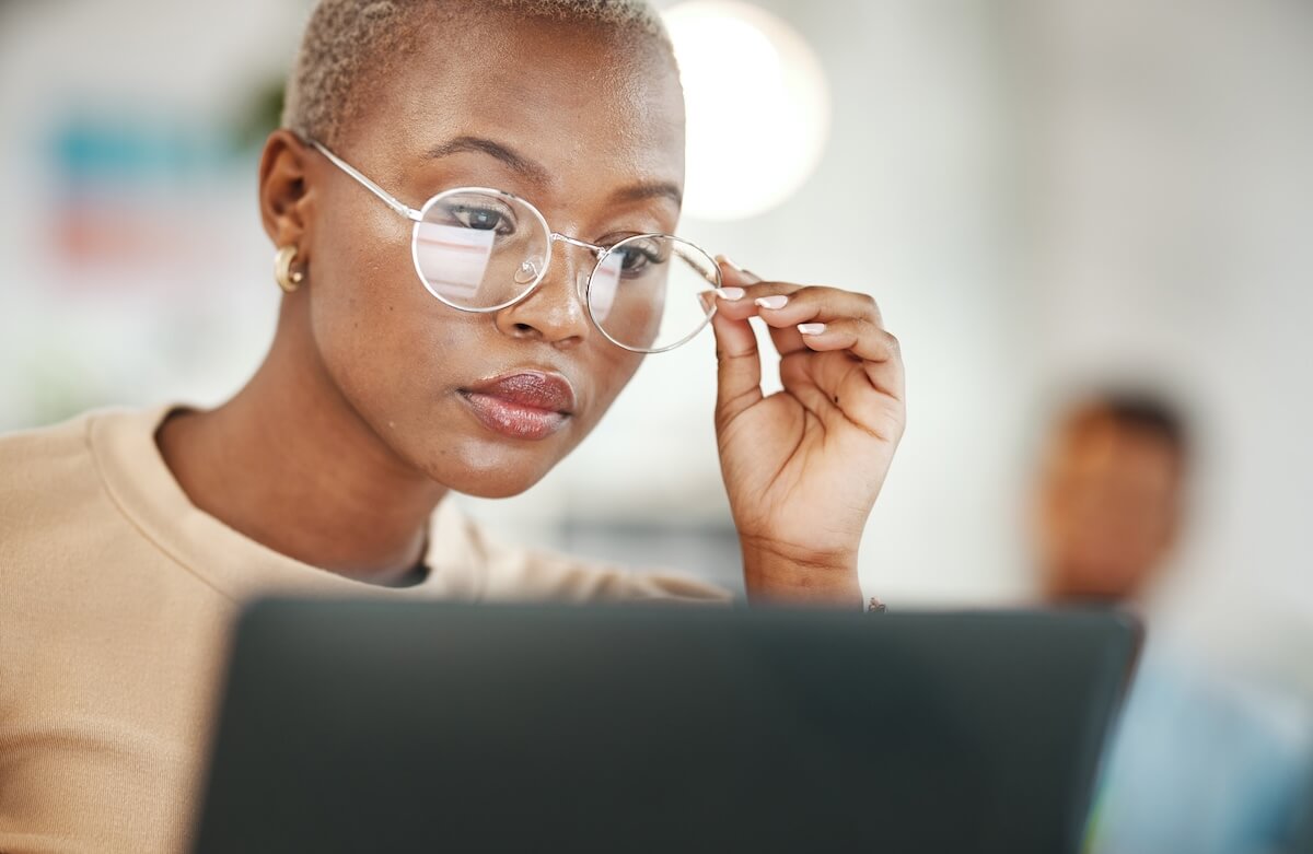 Shutterstock: Office, computer and black woman with glasses, serious or reading email, online research or report. Laptop, concentration and African journalist proofreading article for digital news website or blog
