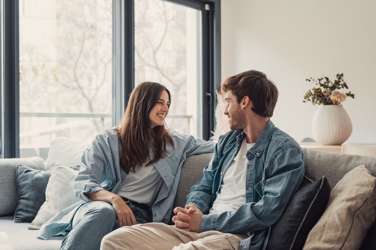 Shutterstock: Young happy couple having fun talking laughing relaxing at home on couch, boyfriend embracing girlfriend telling funny joke sitting on sofa, humor in relationships, enjoying weekend together
