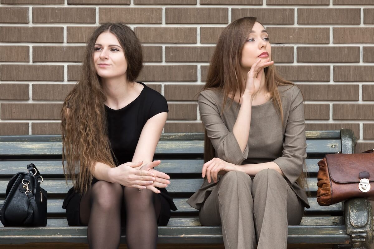 Shutterstock: Full length portrait of two beautiful young female rivals sitting side by side on bench. Attractive caucasian office women holding grudge against each other