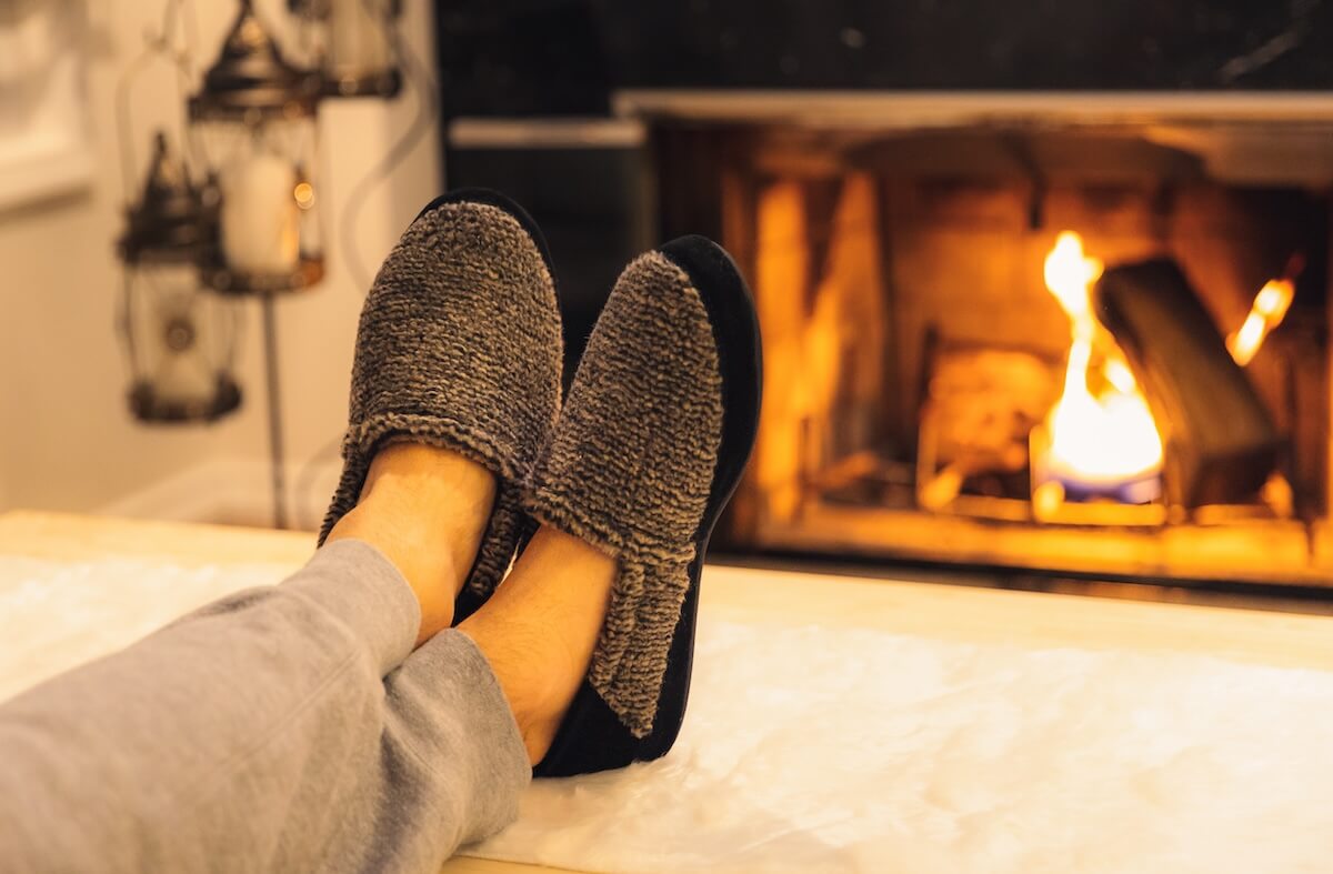 Shutterstock: Man in slippers relaxing with his feet up - warm cozy cabin scene with a fireplace in the background.