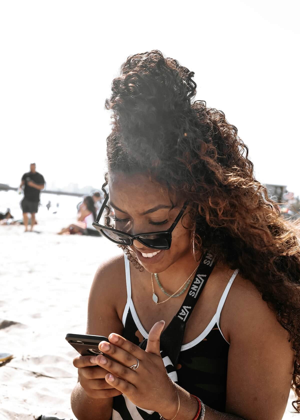 Unsplash: Smiling woman in sunglasses texting at beach by Kevin Turcios