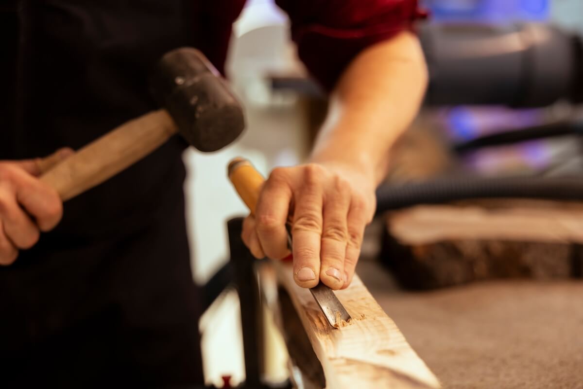 Shutterstock: Man carving intricate designs into wood using chisel and hammer in carpentry shop, enjoying diy hobby. Woodworking specialist in studio shaping wooden pieces with tools, making wood art, close up shot