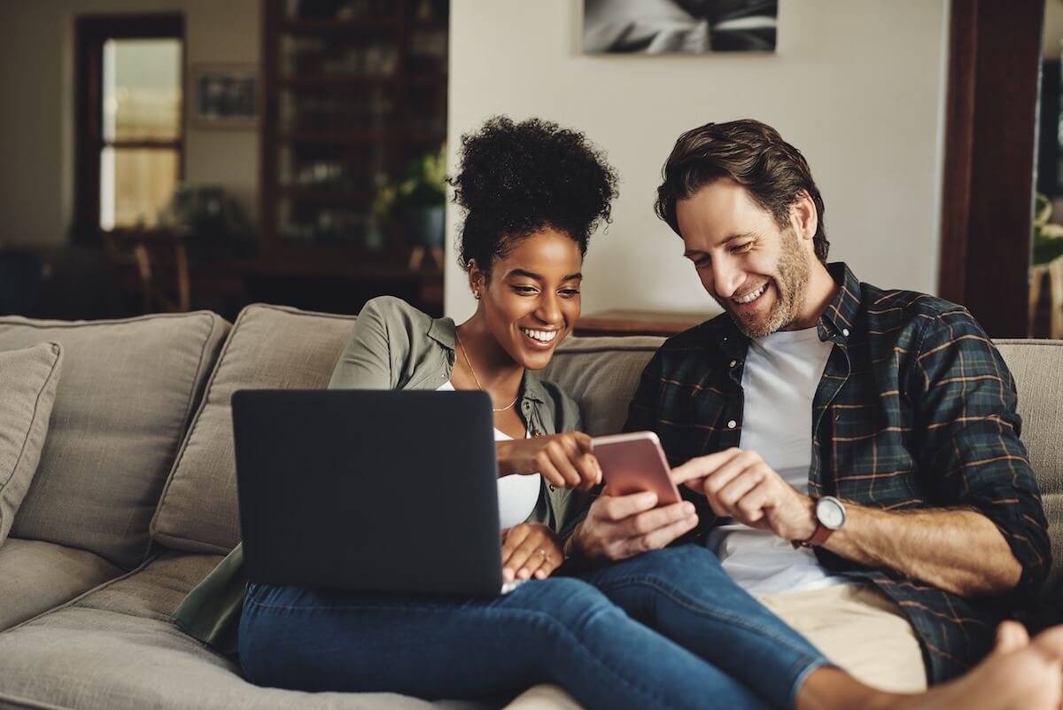 Shutterstock: Couple, relax and happy with technology on sofa for social media, streaming subscription and online shopping for apartment. Man, woman and together in home with laptop or smartphone for connectivity.