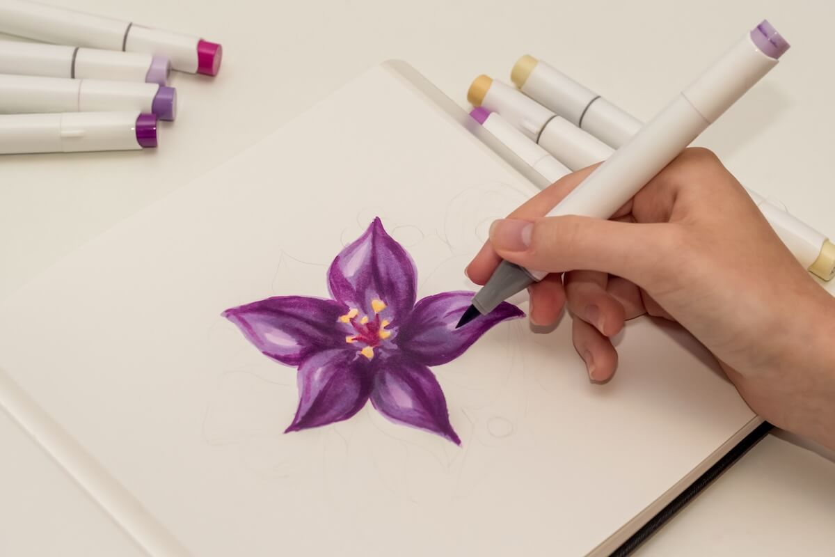 Shutterstock: Hand drawing a purple flower sketch in a sketchbook with alcohol based sketch drawing markers. Learn to sketch