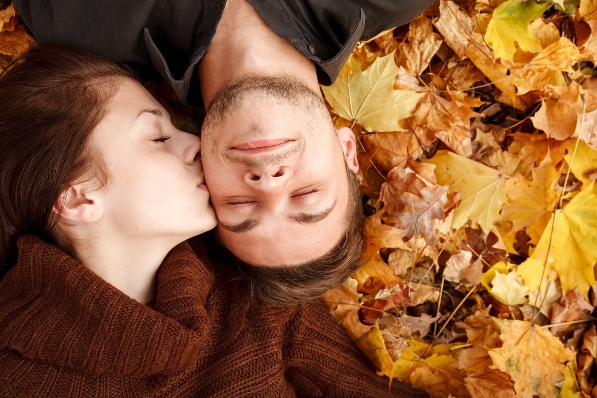 Shutterstock: young couple lying down on autumn leaves eyes closed she kissing him