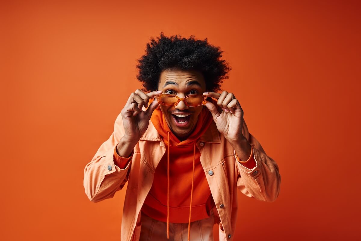 Shutterstock: A stylish, young African American man in an orange jacket holds a pair of glasses against an orange background.
