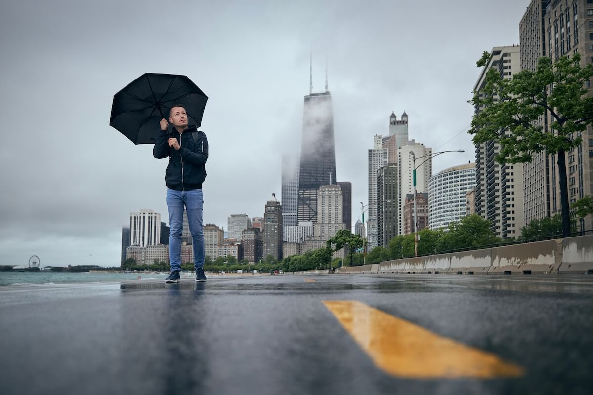 Shutterstock: Man with umbrella walking against Chicago cityscape. Rainy and windy day in city.