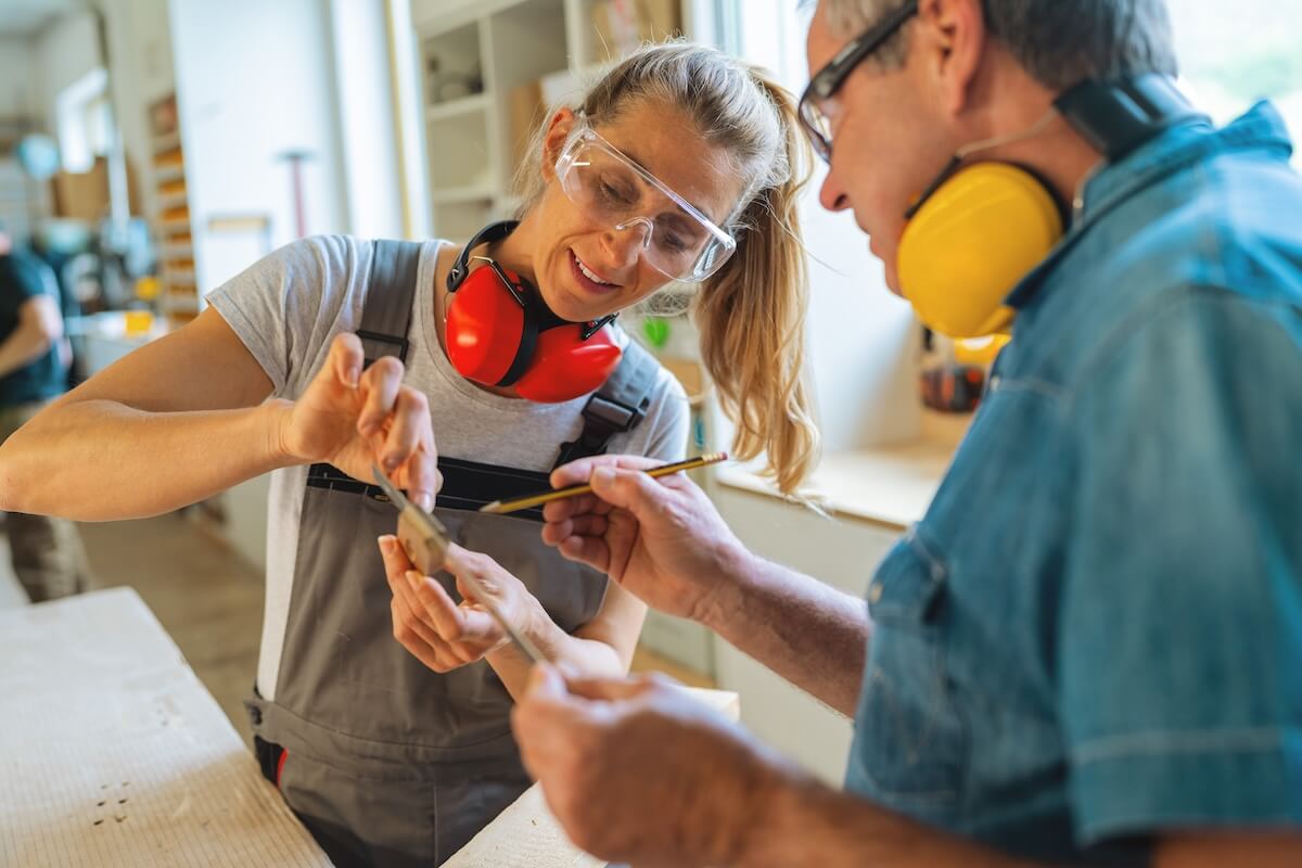 Shutterstock: Carpentry mentor and apprentice measuring a wooden piece in a well-lit workshop