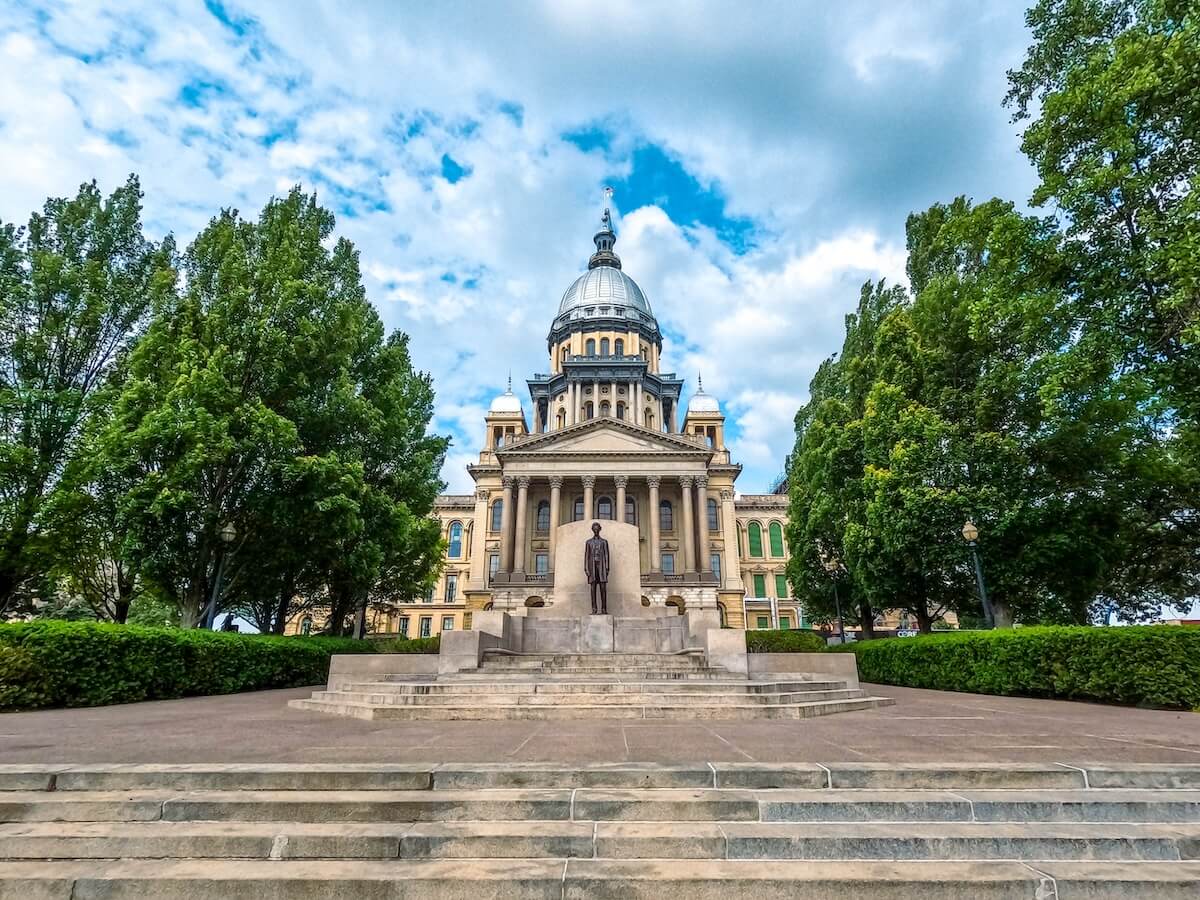 Shutterstock: Springfield, Illinois, USA : May 20, 2024 Front view of the Illinois State Capitol Building. Bronze statue of Abraham Lincoln stands tall in front of the majestic building. Cloudy blue skies overhead