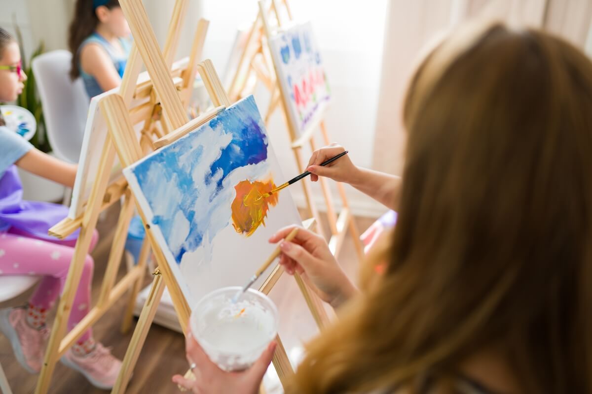 Shutterstock: Art teacher helping young students painting on canvas during art class at school using brushes and tempera colors