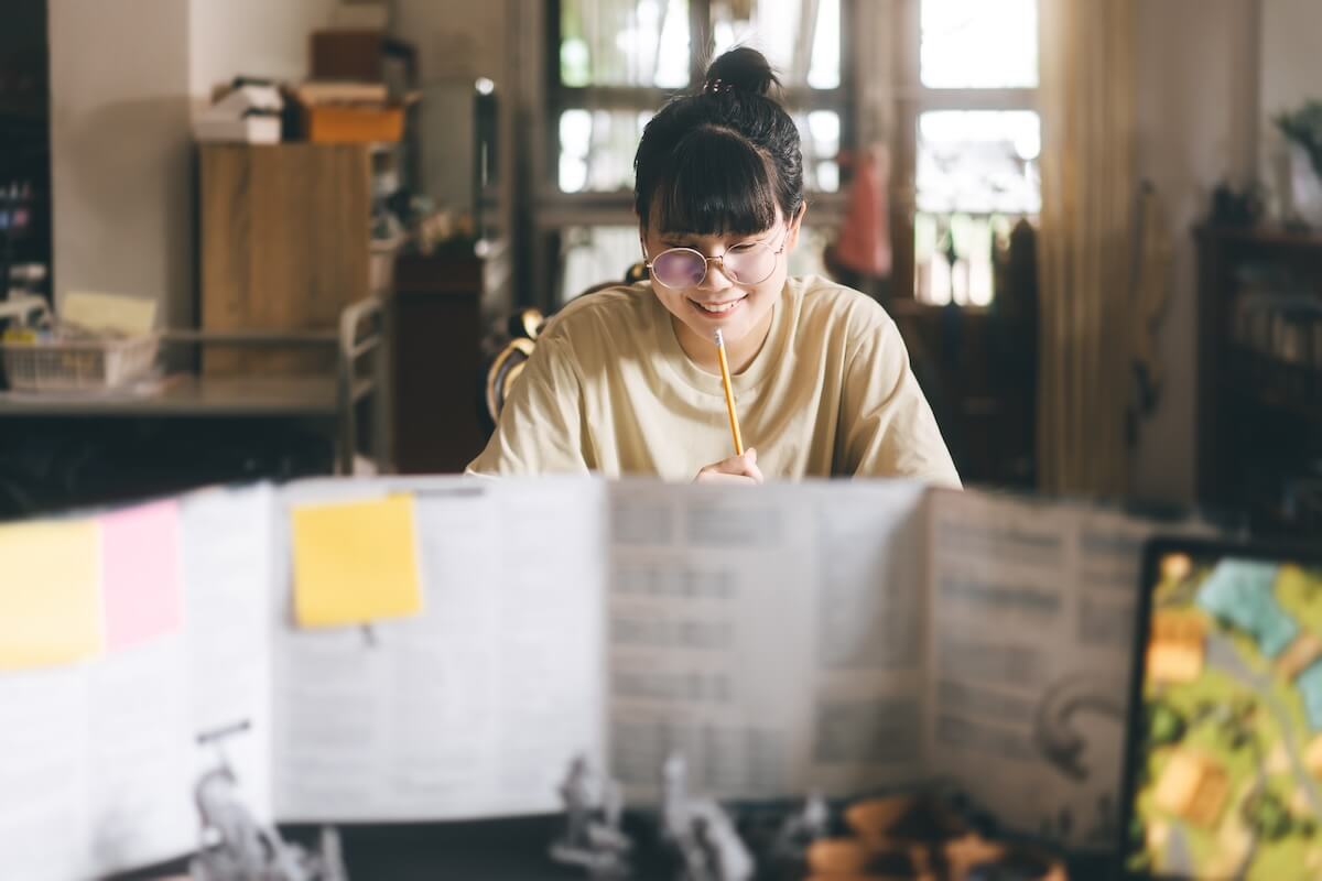 Shutterstock: Role playing tabletop and board games hobby concept. Young adult asian woman enjoying with storytelling. Blur foreground with dungeon master screen and monster miniatures.
