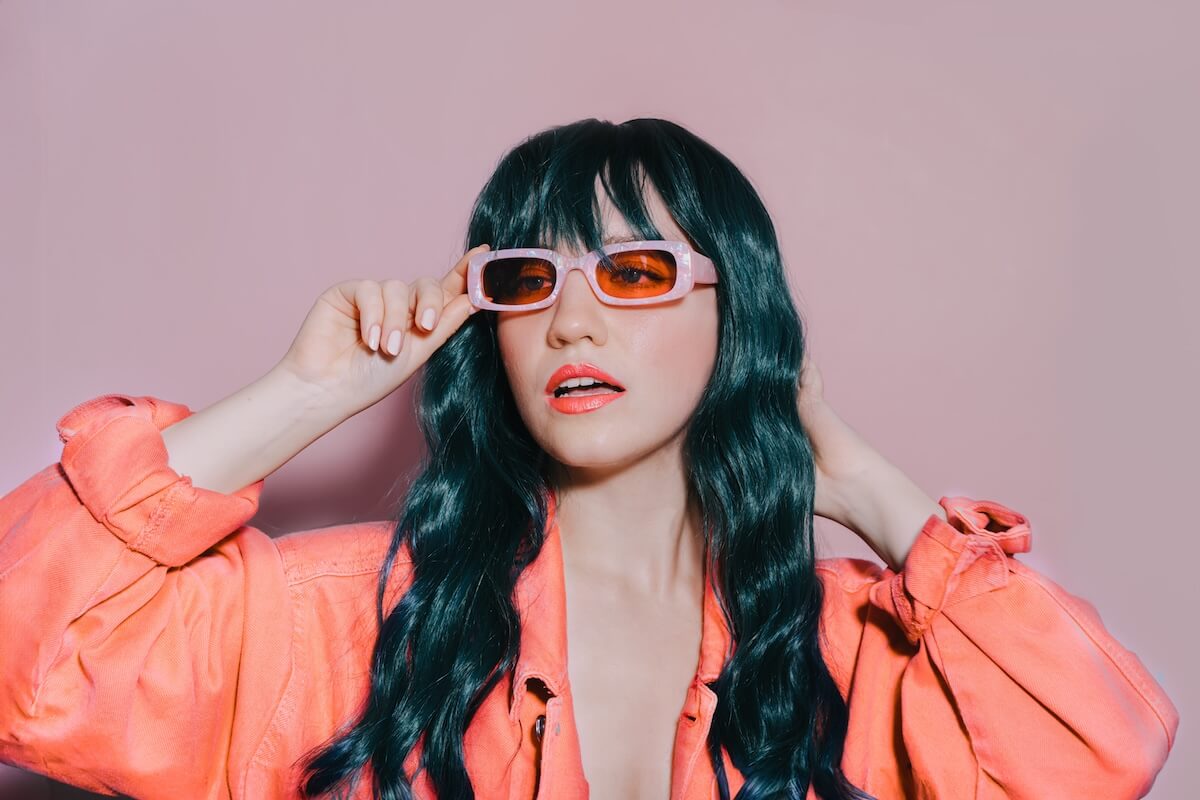 Shutterstock: Bright fashion portrait of young woman with long green color hair, and trendy peach color lips, jacket and sunglasses on pink background. Stylish hairstyle, makeup. Sexy Model, Color of the 2024 year.