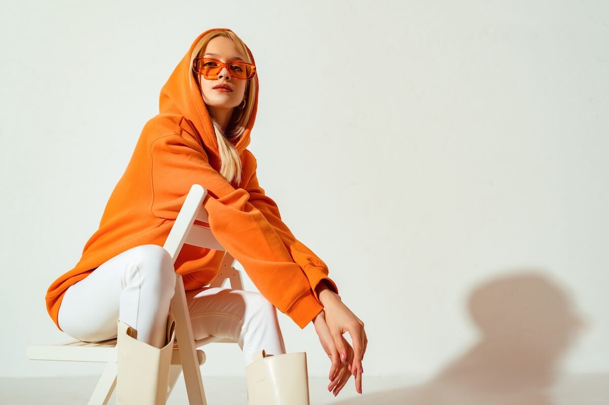 Shutterstock: Young confident blonde girl wearing trendy orange hoodie, color sunglasses, posing on white background. Studio fashion portrait. Copy, empty space for text