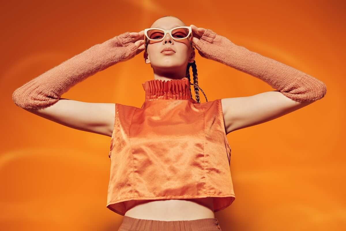 Shutterstock: Summer Fashion style. Portrait of a beautiful fashion model girl in an orange top and sunglasses on an orange studio background. Soft orange makeup and braided hairstyle.