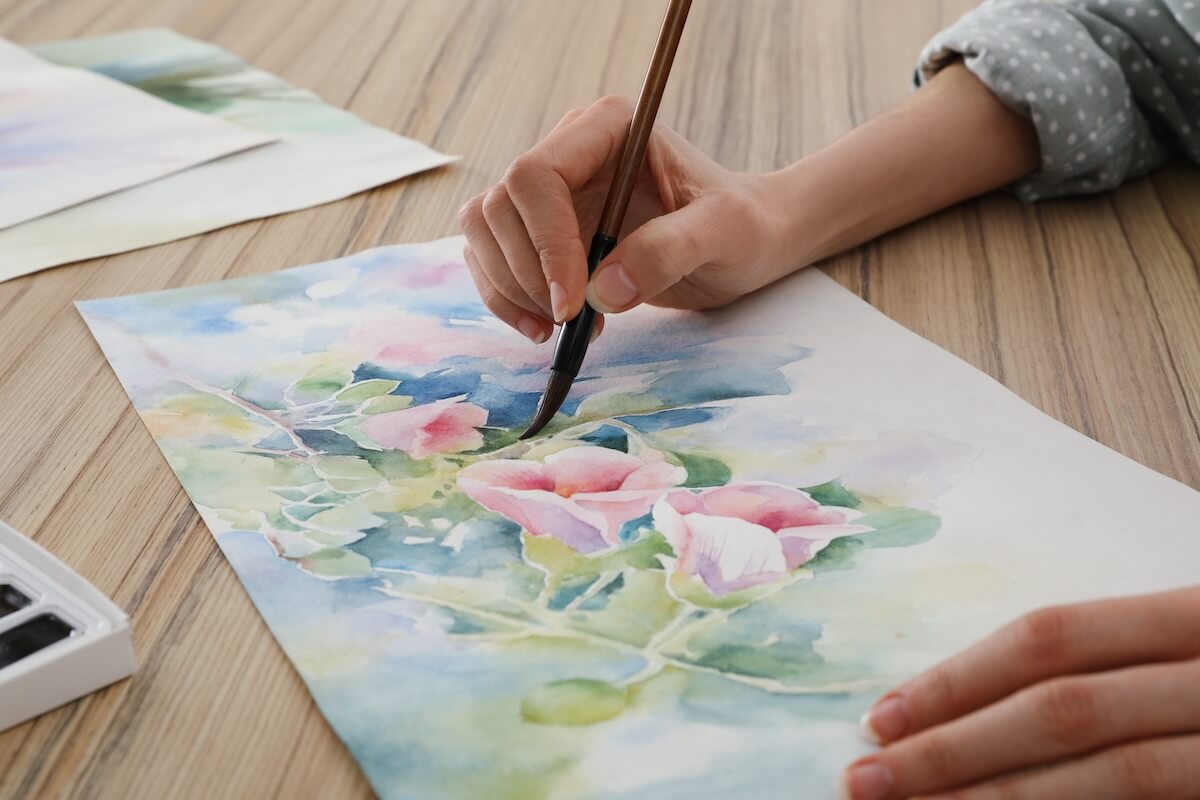 Shutterstock: Woman painting flowers with watercolor at wooden table, closeup. Creative artwork