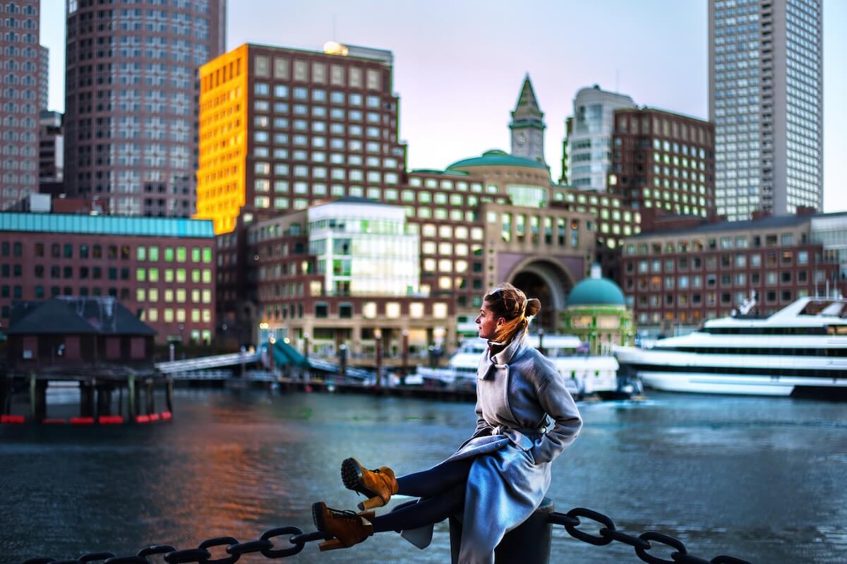 Shutterstock: girl in coat against the backdrop of the cityscape yachts and riverboats moored in Boston harbor