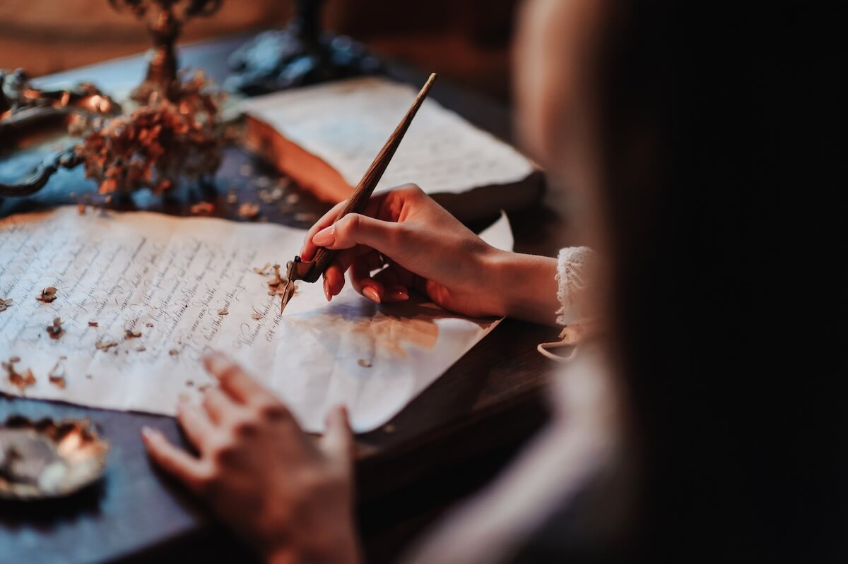 Shutterstock: Girl writes a letter with an antique fountain pen. A female hand holds a pen over a sheet of paper in the light of a candle.