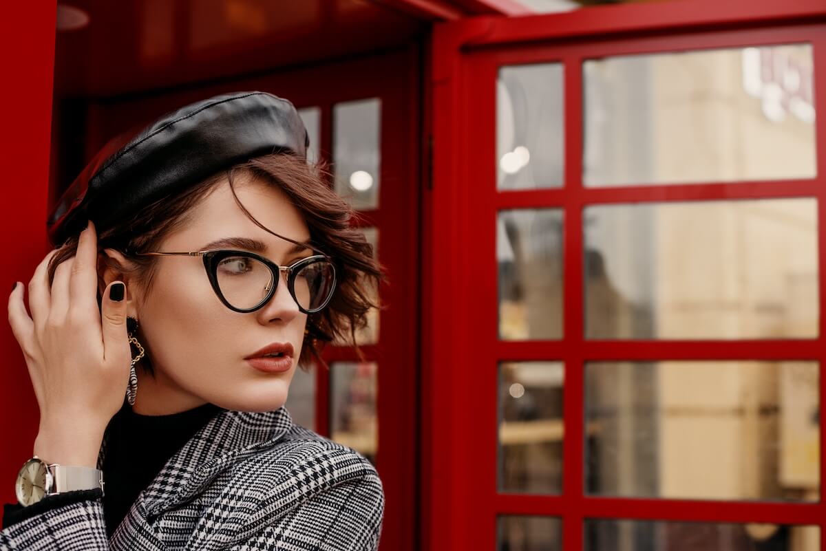 Shutterstock: Fashionable, elegant woman wearing glasses, trendy leather beret, hand watch, classic autumn coat, posing near red call box in street of city. Copy, empty space for text