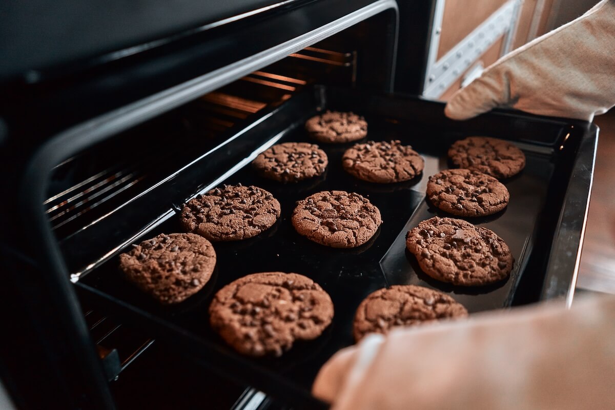 Shutterstock: Close up of hands taking out a baking sheet from the oven with cookies with chocolate. Baking process concept
