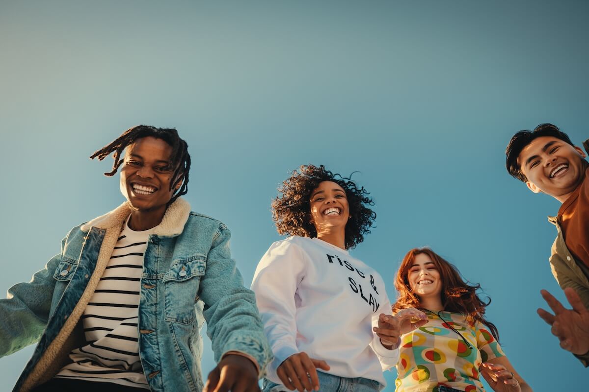 Shutterstock: Group of happy young friends having fun outdoors, enjoying sunny day under blue sky. Joyful Gen Z people embracing friendship and laughter.