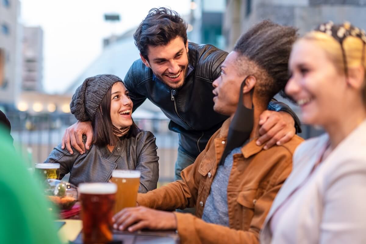 Shutterstock: multi ethnic group of students chatting around a table in a brewery, gathering of young people during afternoon hours due curfew, restrictive health measures to prevent the spread of the corona virus