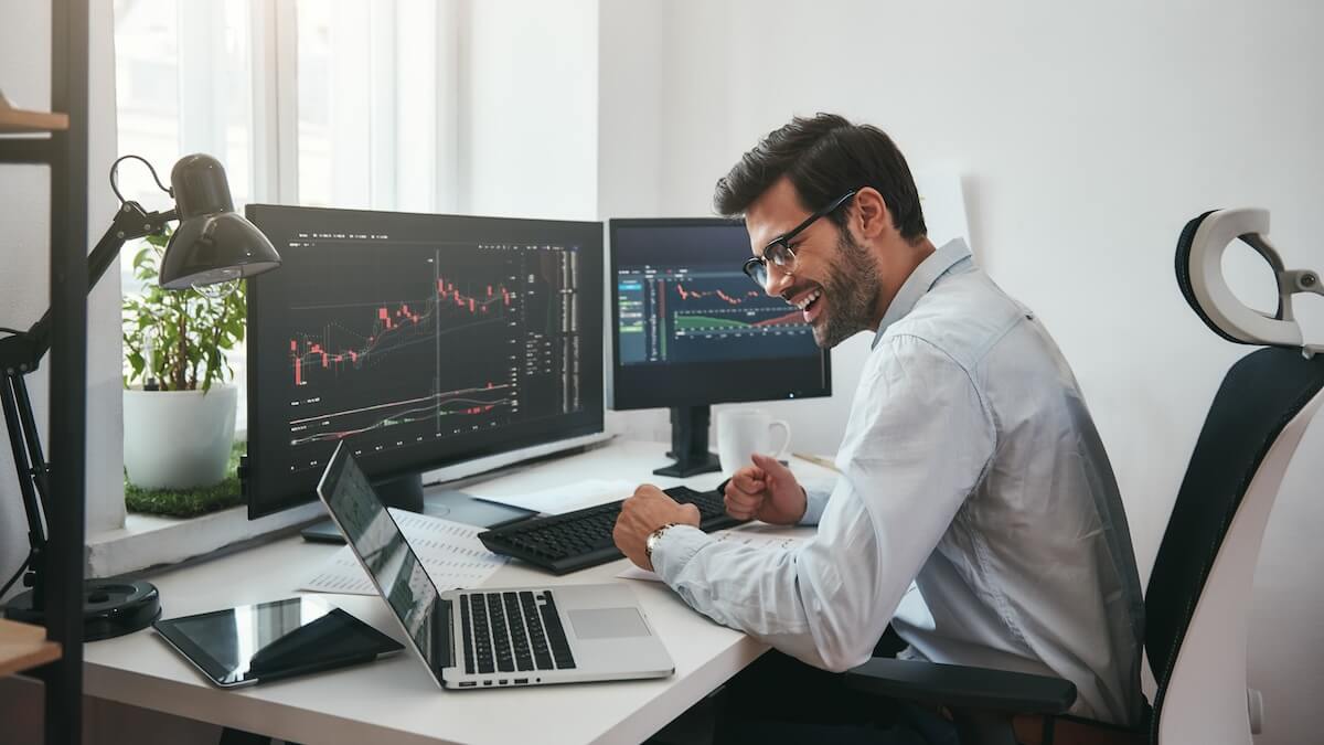 Shutterstock: Lucky day. Happy young businessman or trader in formalwear and eyeglasses using laptop and smiling while sitting in his modern office