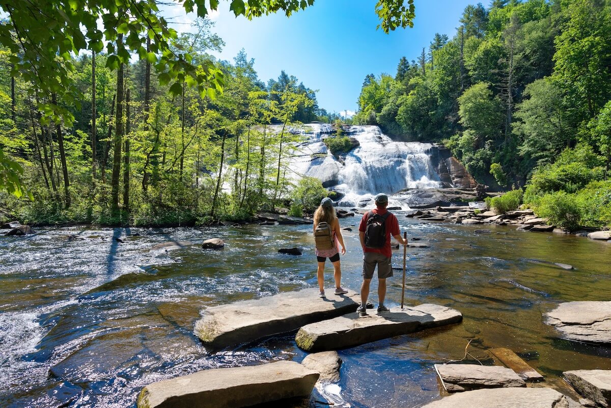 Shutterstock: Couple standing on the rock enjoying beautiful waterfall view.Friends relaxing on hiking trip.High Falls of Dupont State Forest in Brevard. Blue Ridge Mountains, near Asheville, North Carolina, USA.