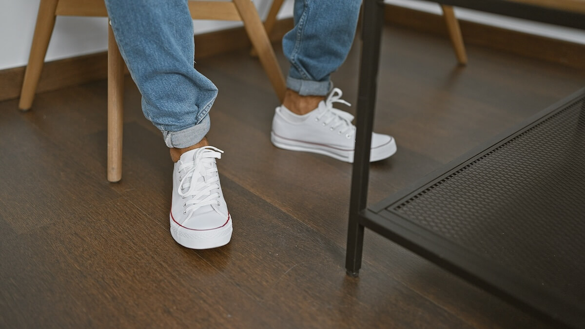 Shutterstock: Casual man wearing jeans and white sneakers sitting on a wooden chair in a modern indoor room.