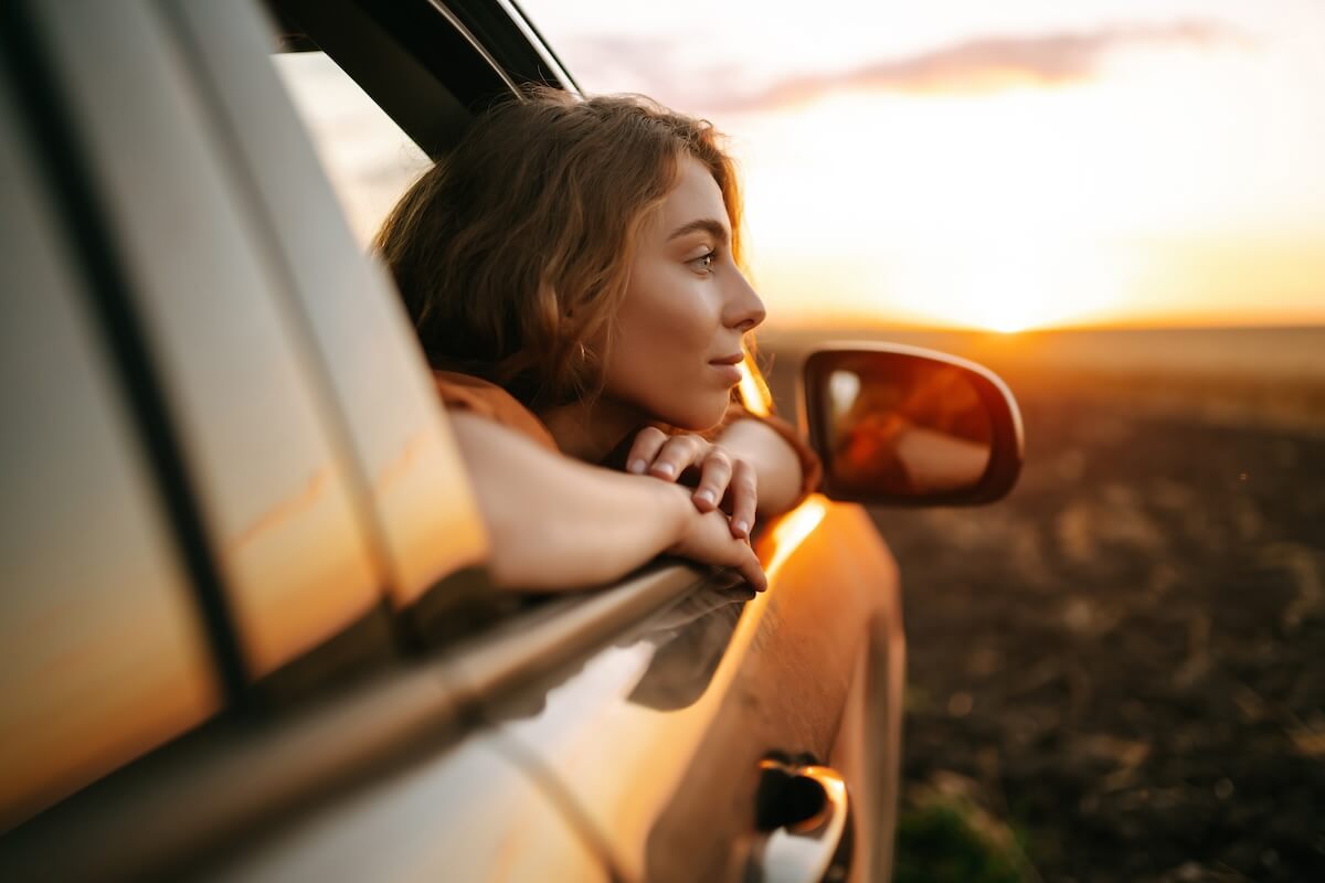 Shutterstock: Happy woman outstretches her arms while sticking out the car window. Lifestyle, travel, tourism, nature, active life.