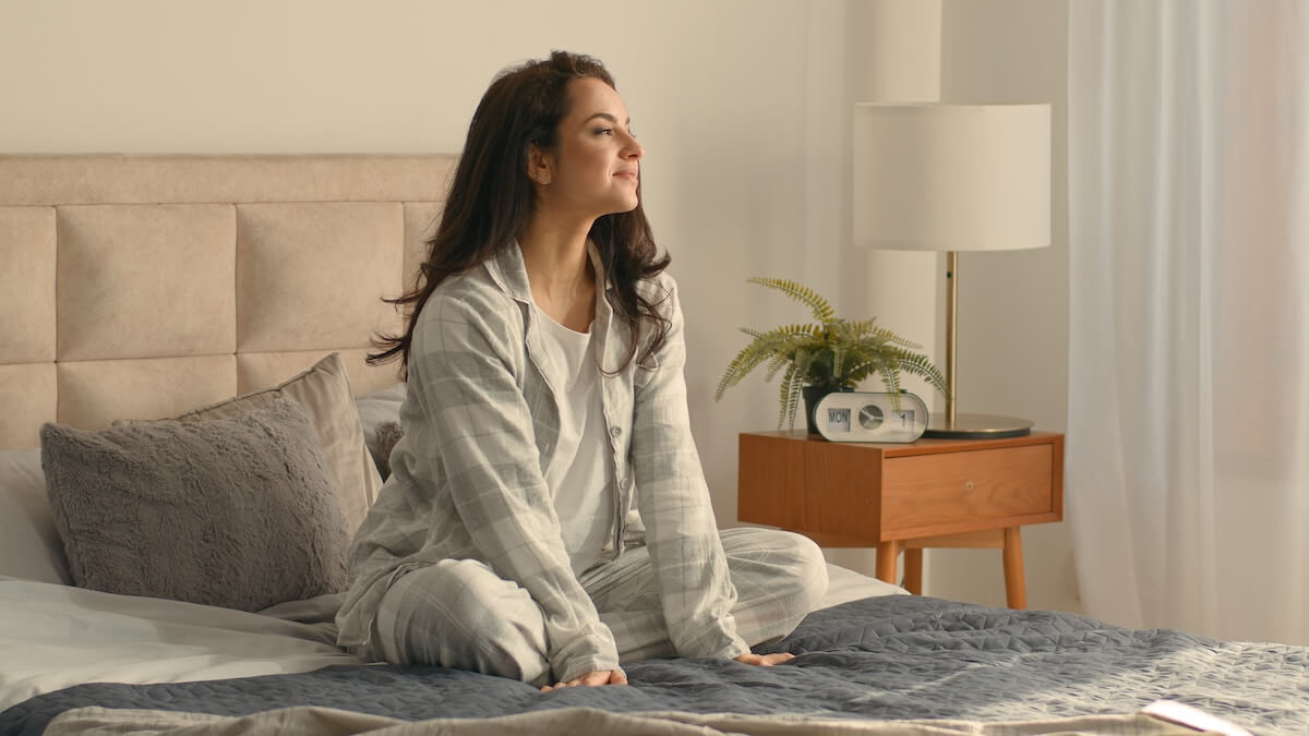 Shutterstock: Caucasian brunette woman sitting on bed bedroom home touching neck massage good morning calm comfortable cozy inside awake healthcare in pajamas relaxing smiling wellbeing peaceful apartment recovery