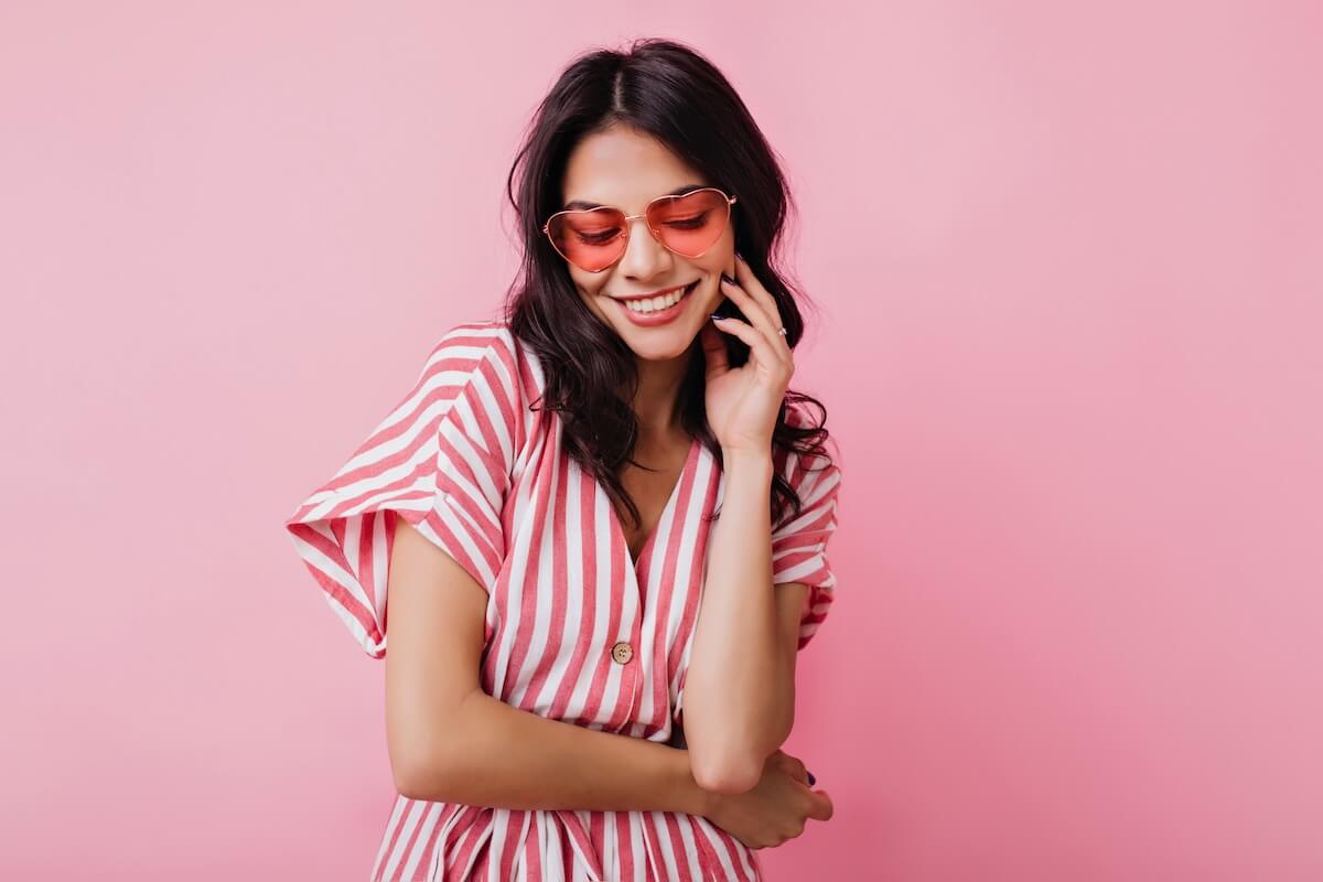Shutterstock: Romantic brown-haired girl in trendy heart glasses posing with shy smile. Indoor photo of graceful young woman in summer attire and accessories.