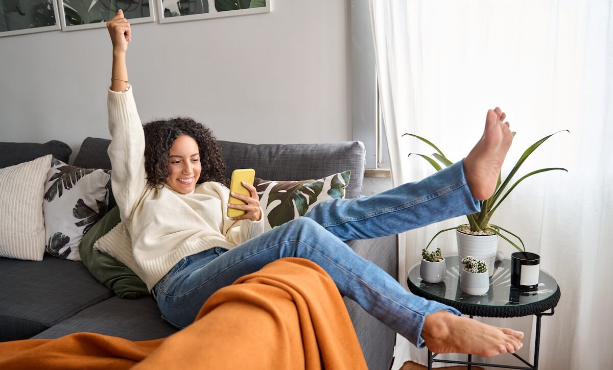 Shutterstock: Happy excited young latin woman relaxing on couch using phone winning money in online app game. Young lucky woman feeling winner looking at cellphone, receiving great news or discount offer.