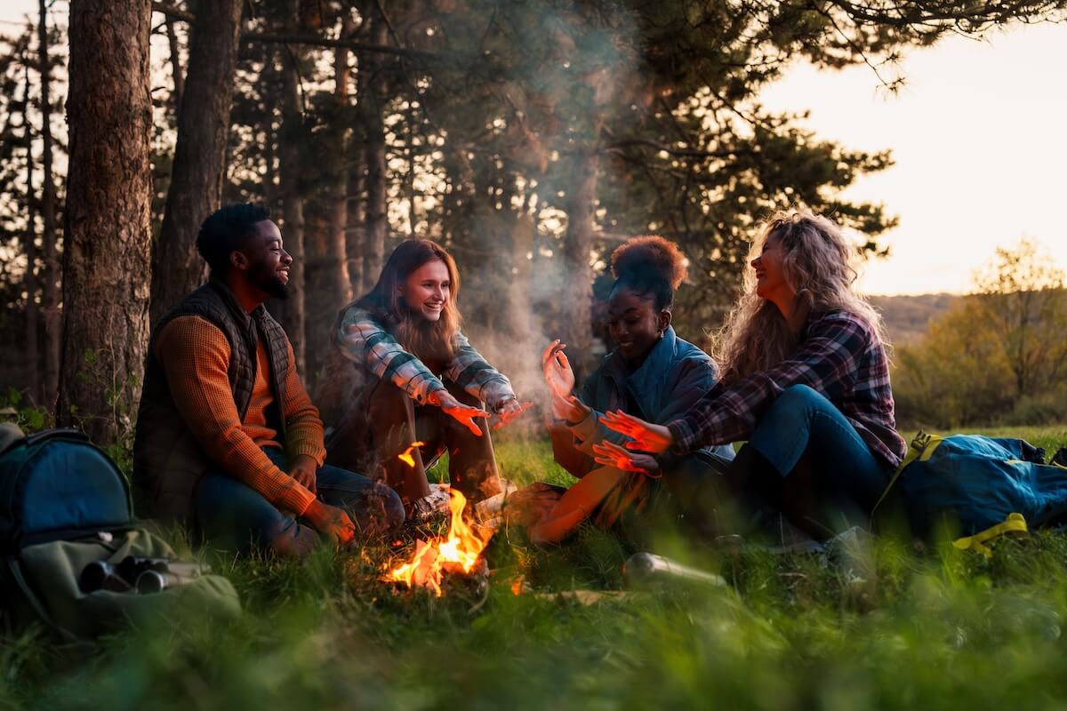Shutterstock: Group of young hikers sitting around a campfire, warming hands and sharing laughter while enjoying engaging conversations during a camping trip in the forest at dusk